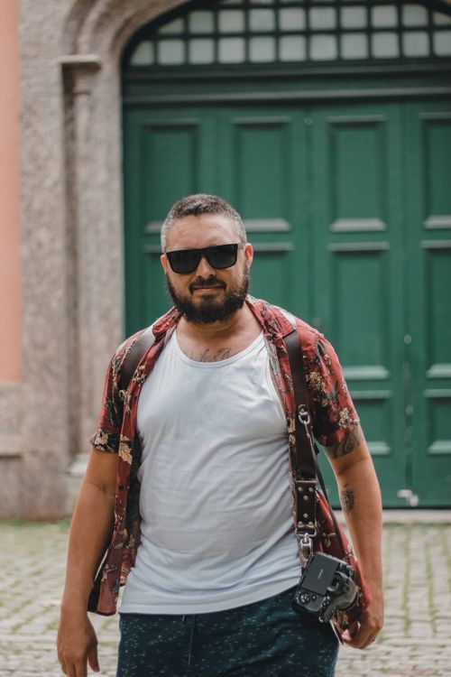 Free A bearded man wearing sunglasses and holding a camera in an urban setting. Stock Photo