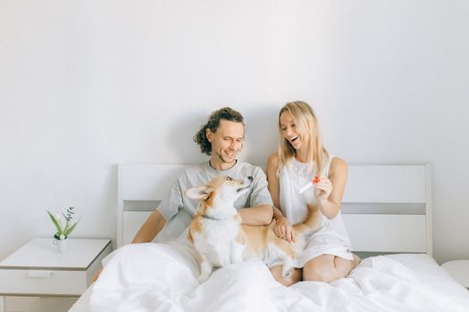 一对快乐的夫妇和他们的柯基犬在床上庆祝妊娠检测呈阳性，表达着爱与兴奋