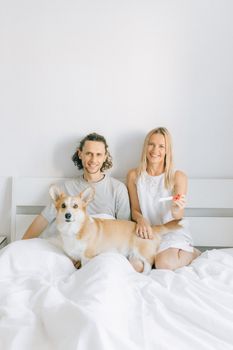 一对微笑的夫妇和他们的柯基犬躺在床上，手里拿着显示阳性的验孕棒，象征着爱与新的开始