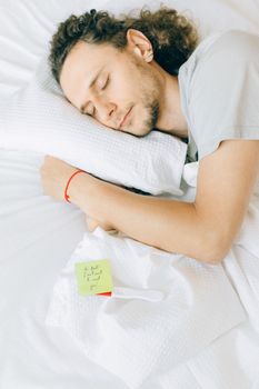 一名卷发男子在床上安详地睡着，旁边放着一张纸条，营造出宁静舒适的氛围