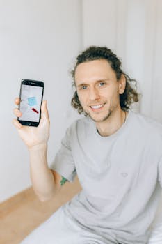 Man smiling while holding a smartphone displaying a note app, indoors.