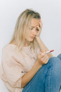一名忧心忡忡的妇女拿着验孕棒坐在室内，神情中透露出不确定