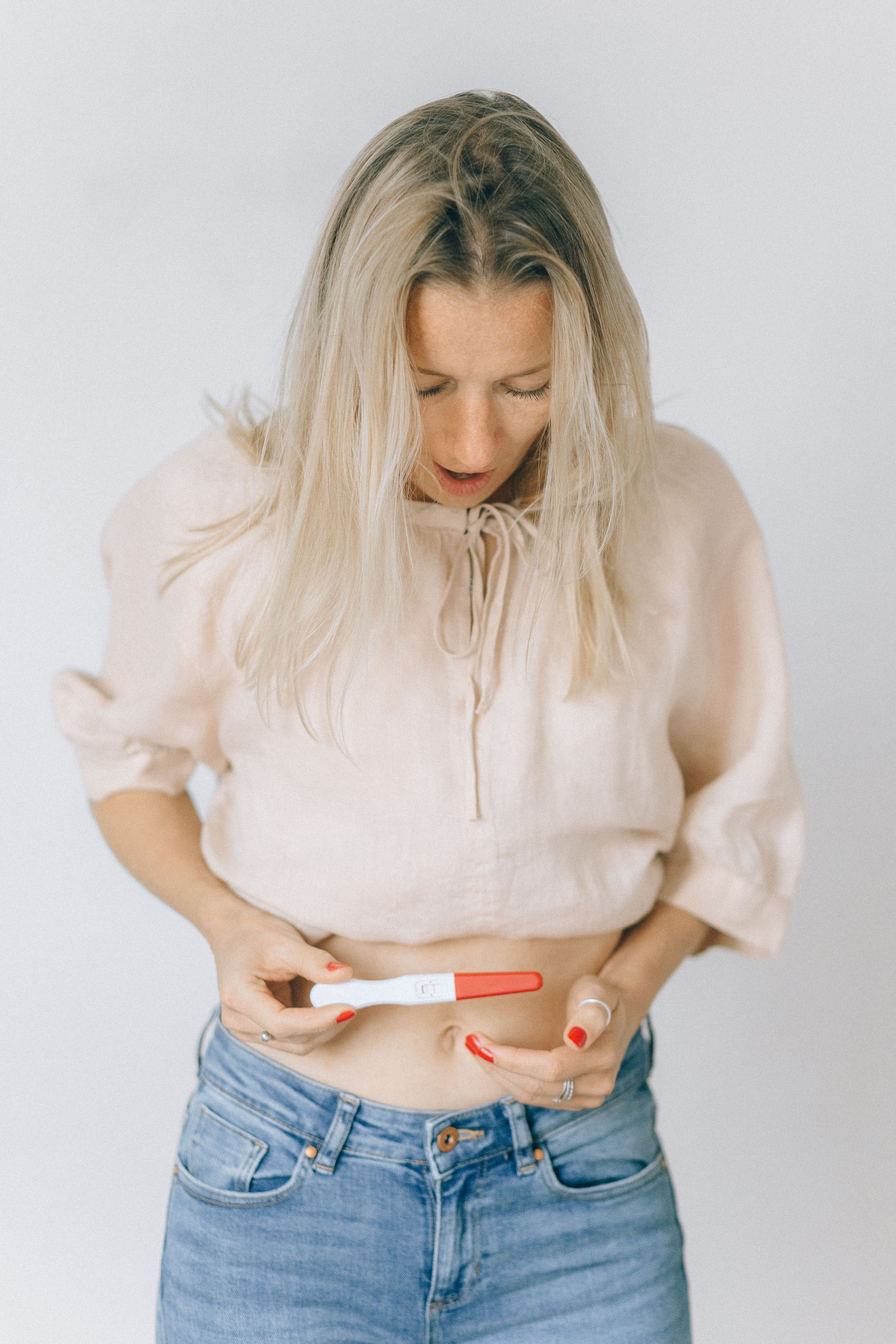 一位穿着休闲装的白人妇女看着呈阳性的妊娠测试，若有所思
