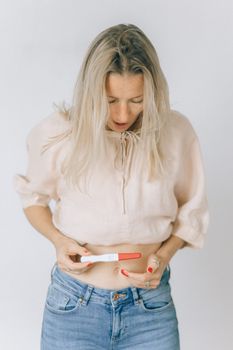 一位穿着休闲装的白人妇女看着呈阳性的妊娠测试，若有所思