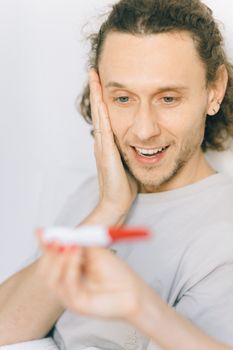 一个快乐的男人卷着头发，对妊娠测试呈阳性感到兴奋