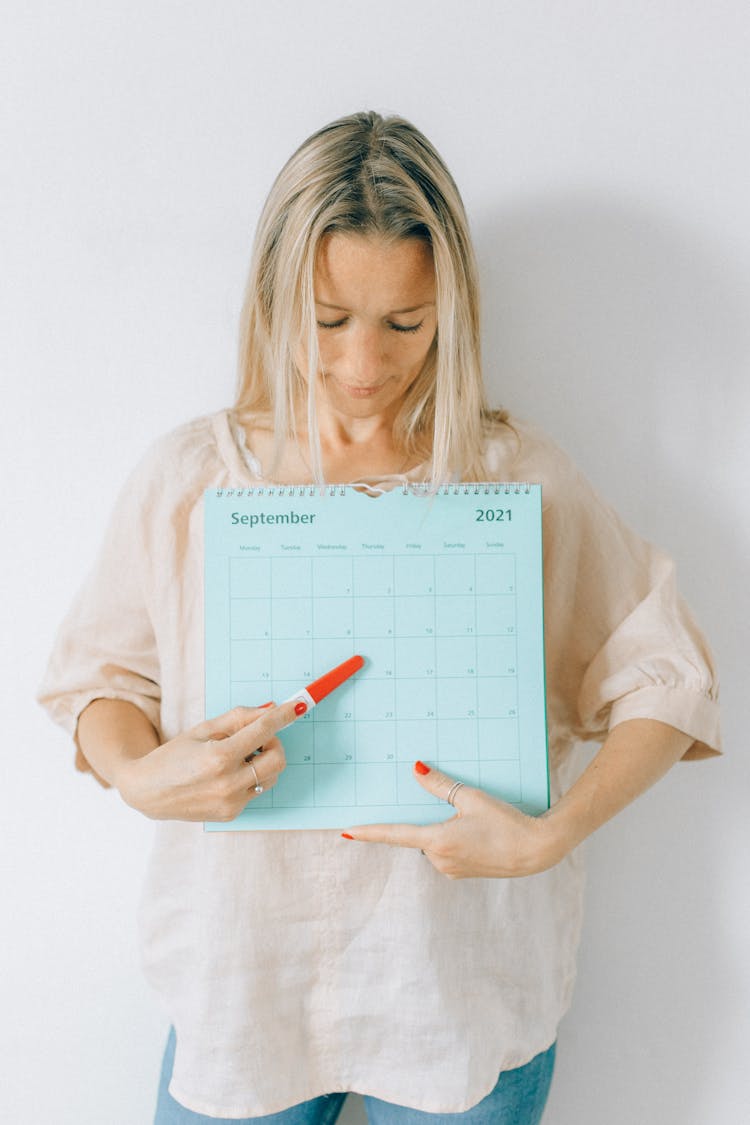 A Woman Pointing A Pregnancy Test At A Calendar