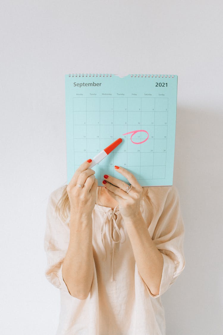 A Woman Pointing A Pregnancy Test At A Calendar