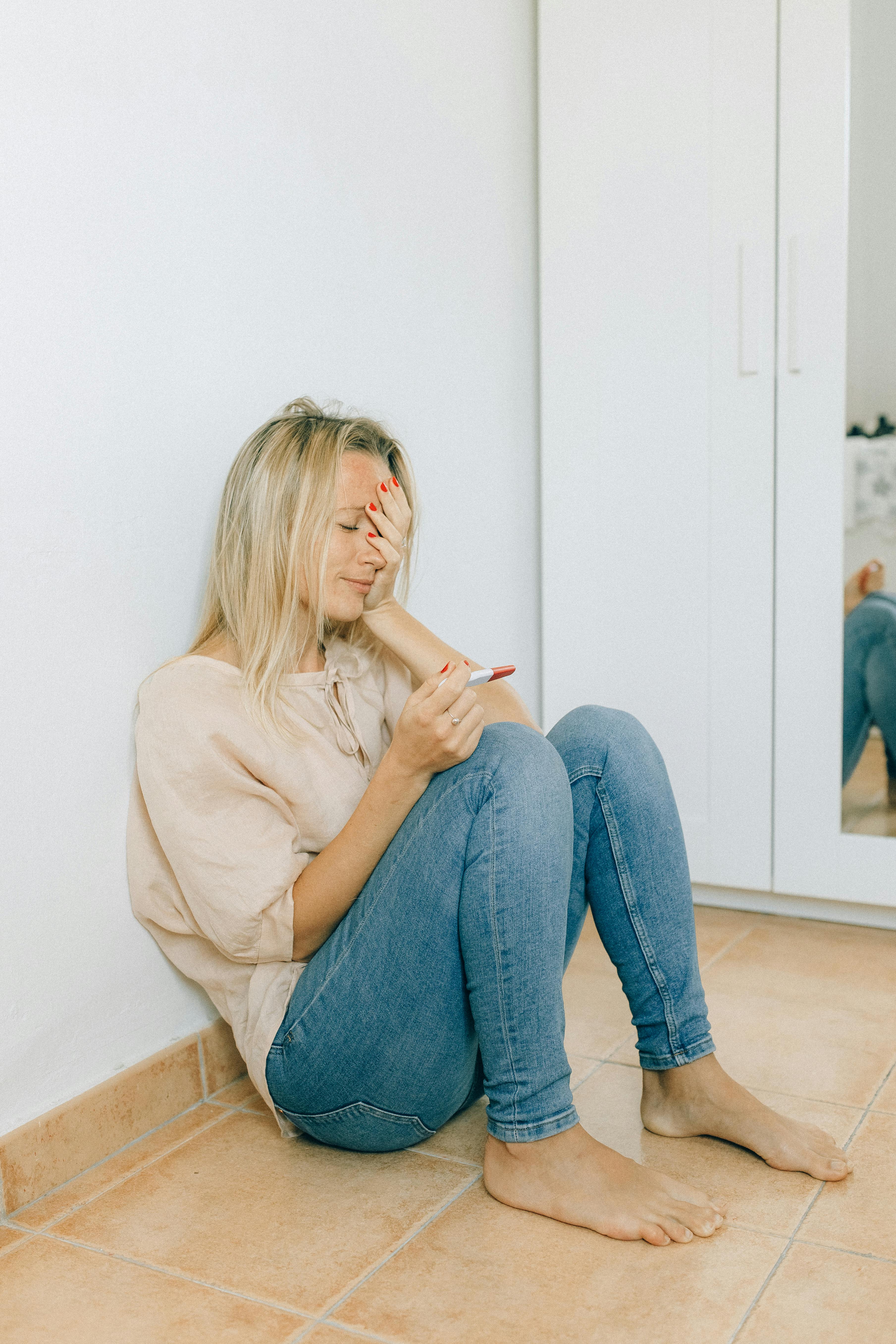 A young woman with a worried expression holds a pregnancy test indoors. Emotional scene.