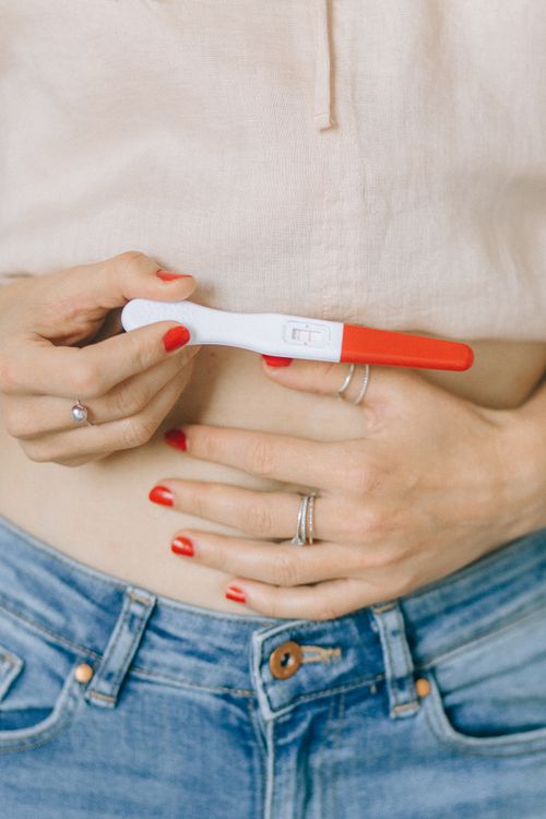 Free Close-up of a woman's hands holding a pregnancy test, showcasing red nail polish and rings. Stock Photo