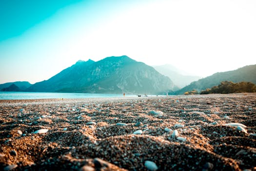 A picturesque beach with mountains in the background during sunset, featuring a sandy shoreline, ideal for travel inspiration.