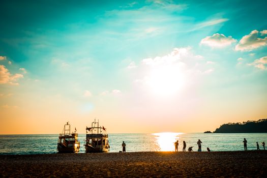 A breathtaking beach sunset with silhouettes of people and boats on the horizon.