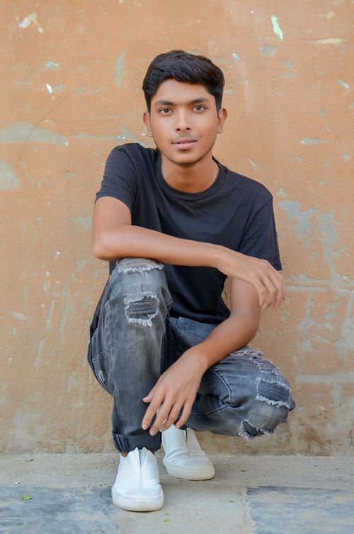 Free A smiling young man in casual attire poses against a textured wall in Karachi, showcasing urban style. Stock Photo