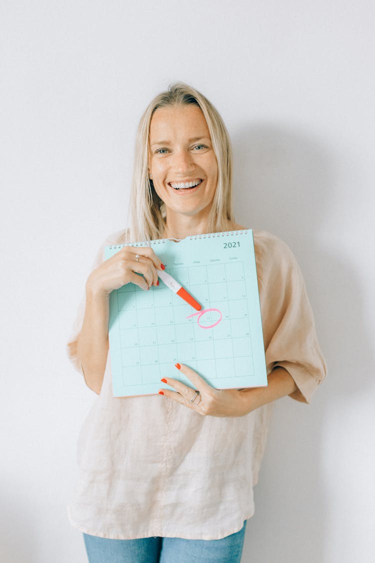 A Woman Pointing A Pregnancy Test At A Calendar