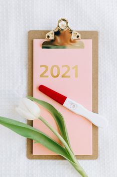 平板电脑上显示着2021年的文本，旁边有妊娠测试棒和郁金香