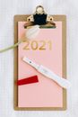 粉红色的剪贴板上平放着验孕棒、郁金香和2021年的标记，象征着新的开始