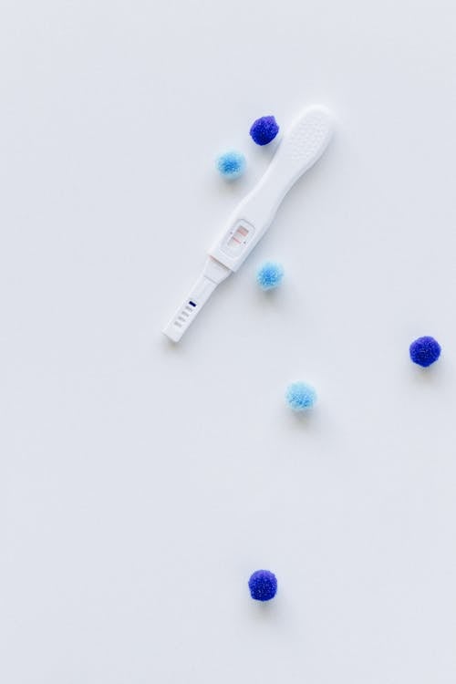 Pregnancy Test and Blue Pom Poms on White Surface