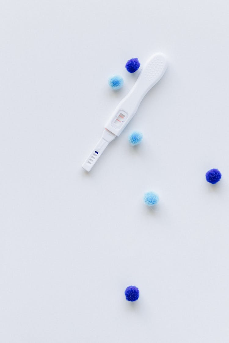 Pregnancy Test And Blue Pom Poms On White Surface