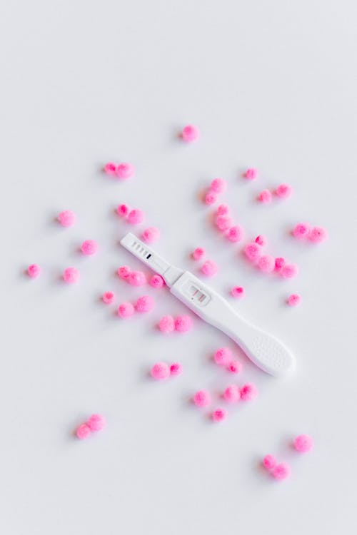 Pregnancy Test and Pink Pom Poms on White Surface