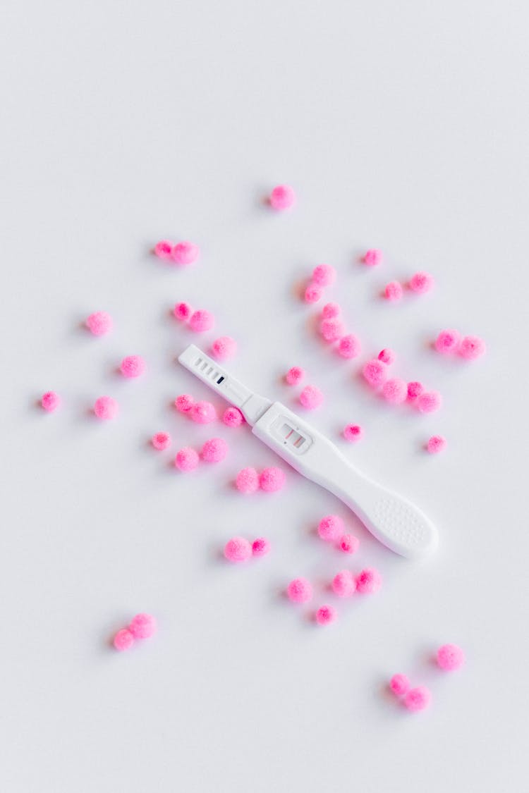 Pregnancy Test And Pink Pom Poms On White Surface