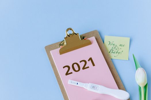 剪贴板上有一张2021年妊娠测试呈阳性的照片，旁边附着一张纸条，写着“你、我和宝贝！”，还画着象征新生命的郁金香