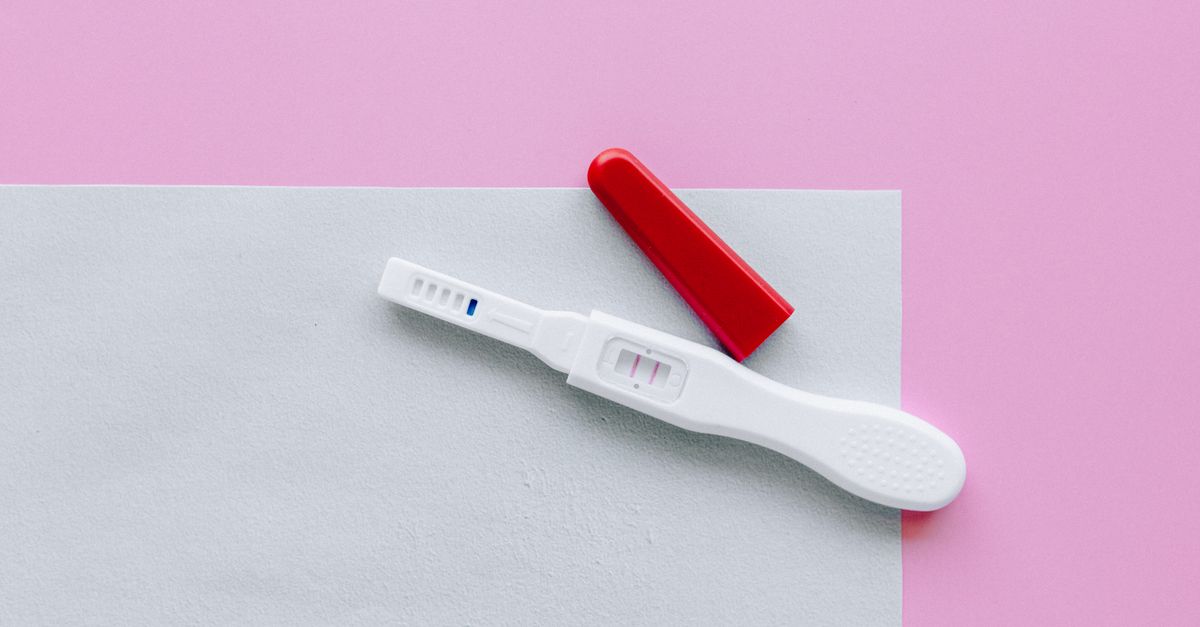 A positive pregnancy test with a red cap on a pink and white surface in a flat lay style.
