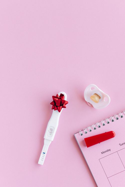 Free Flat lay of pregnancy test with positive result, pacifier, and calendar on pink background. Stock Photo