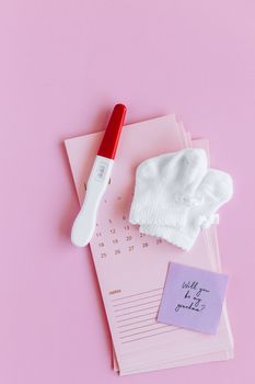 粉色背景上，扁平的妊娠测试棒、婴儿袜和纸条，象征着新的生命