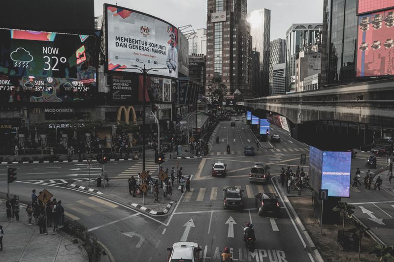 City street view of Kuala Lumpur showcasing traffic and billboards under a cloudy sky.