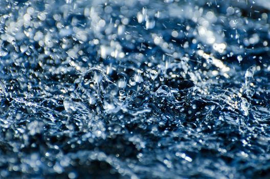 Close-up of water droplets splashing, capturing motion and energy in blue tones.