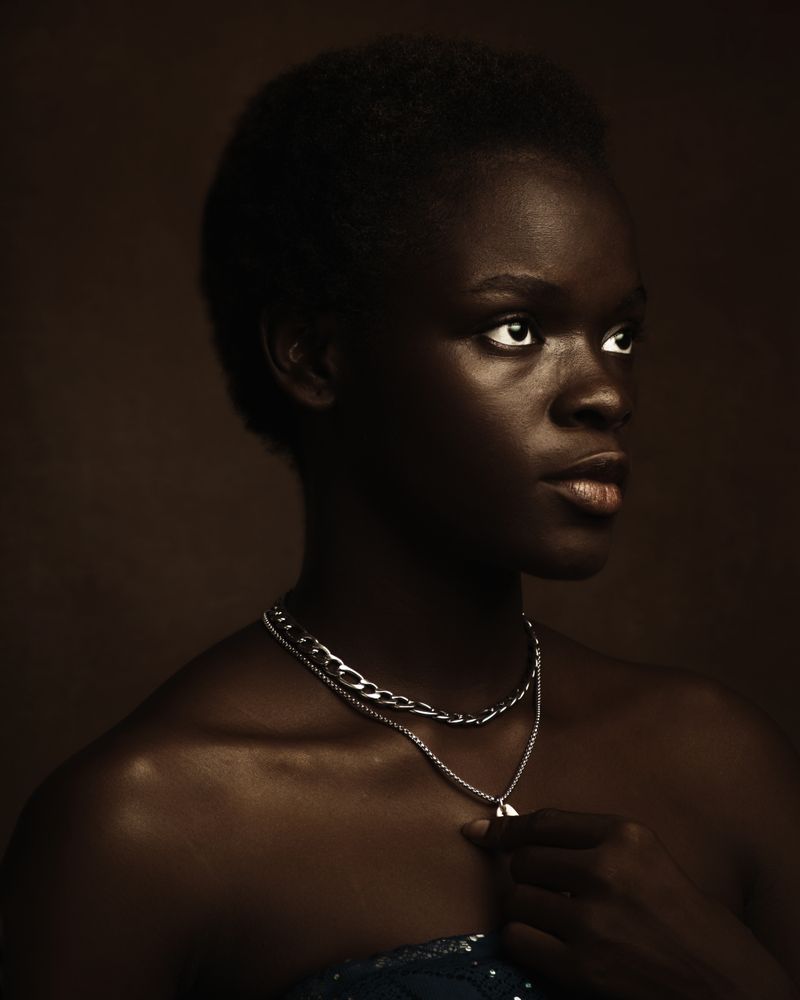 A Black woman photographed in profile against a dark studio backdrop, expression turned inward and pensive, evoking the private weight of intrusive thoughts.
