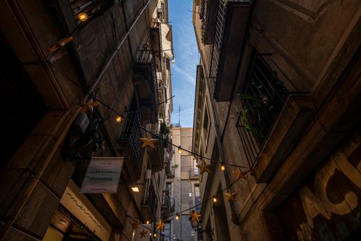 Looking up a narrow alley in Barcelona's Gothic Quarter with string lights and ancient architecture.