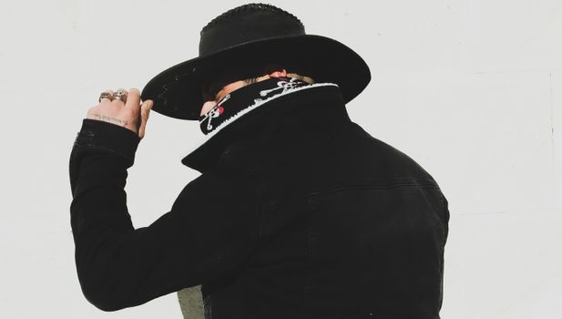 Man in black attire with hat and bandana, exuding mystery and style.
