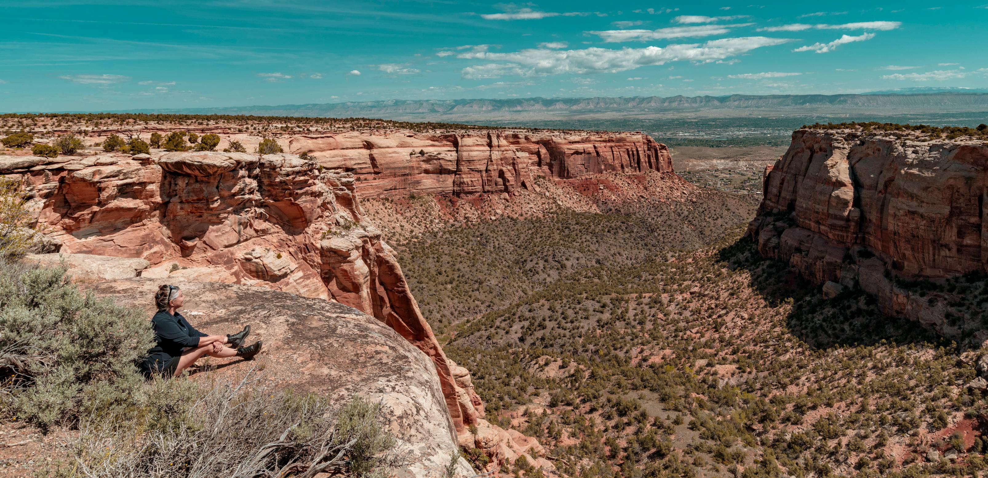 Woman sitting on cliff edge overlooking scenic red rock formations in Fruita, Colorado.