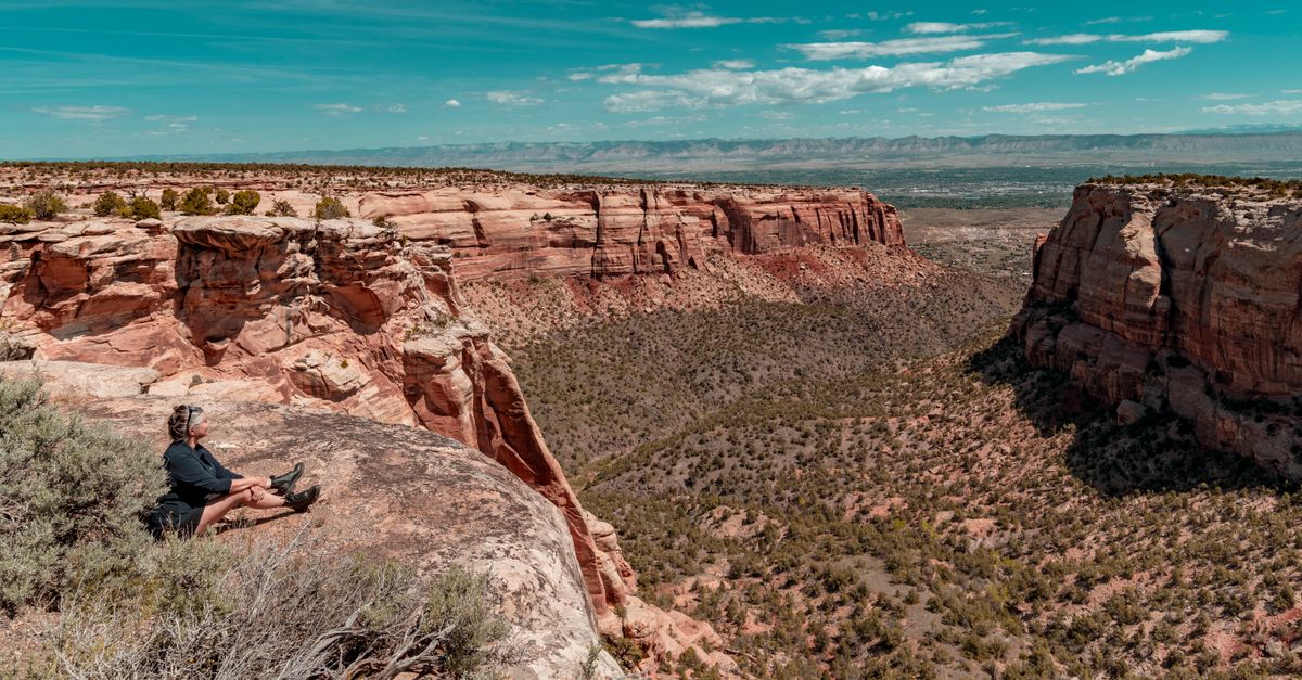 Woman sitting on cliff edge overlooking scenic red rock formations in Fruita, Colorado.