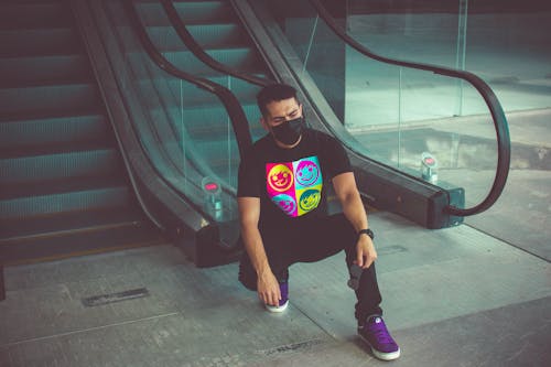 Man With Facemask Sitting Near Escalators 