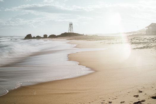 Scenic view of a sunlit beach in NSW, Australia with waves and a lifeguard tower.