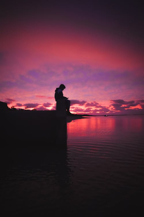 A Silhouette of Man Sitting on a Dock