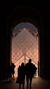 Silhouette of people walking through an archway towards the Louvre Pyramid, Paris.
