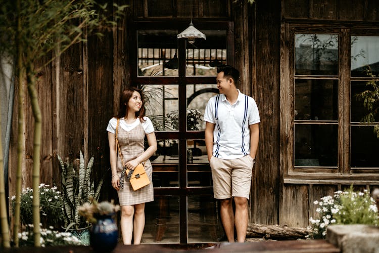 Happy Young Asian Couple Standing Outside Wooden House