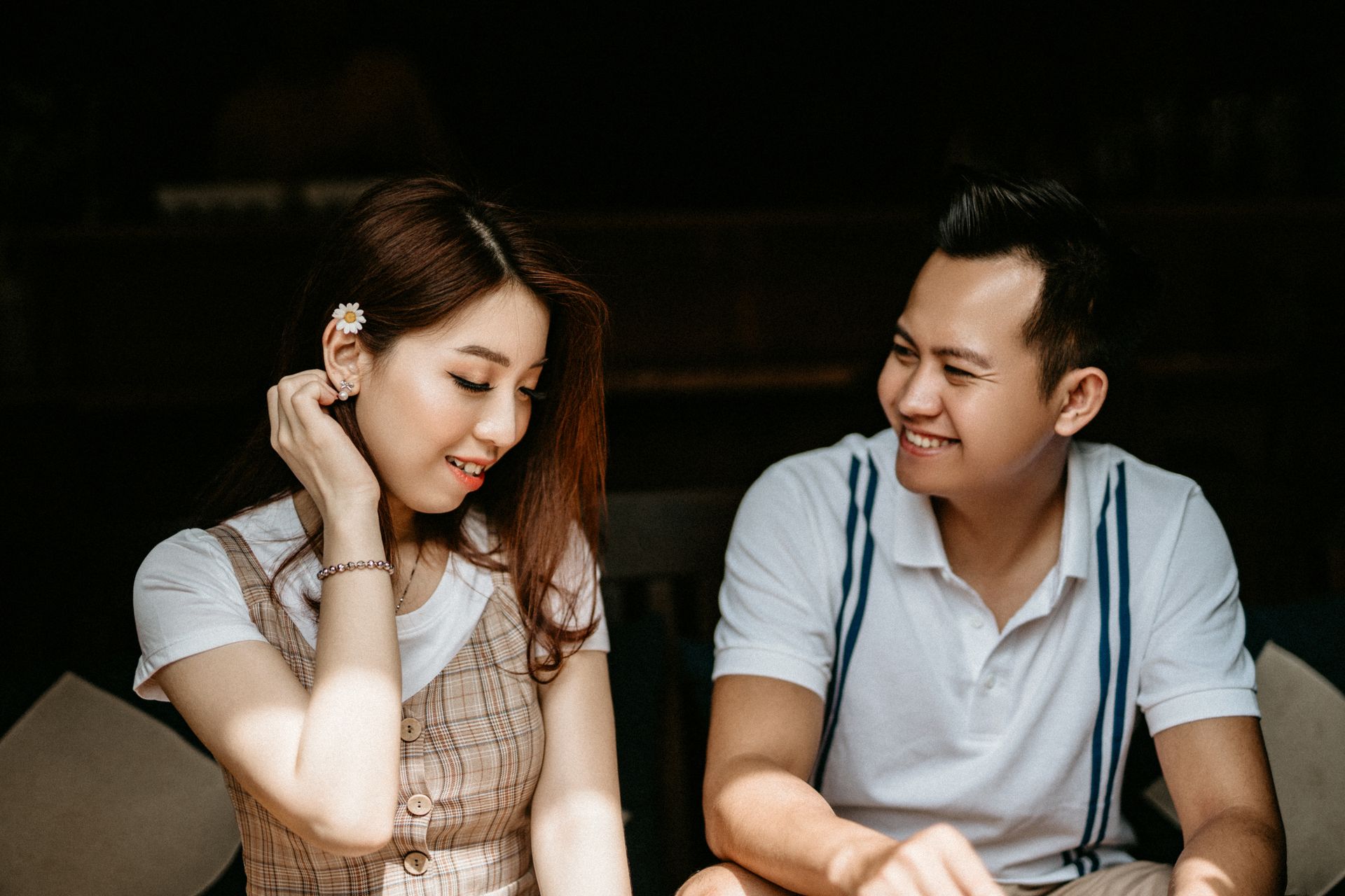 Cheerful Asian couple in casual clothes sitting on sofa having date in cafe and flirting while talking