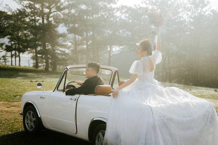 Newlywed Asian Couple Driving Retro Car In Misty Forest