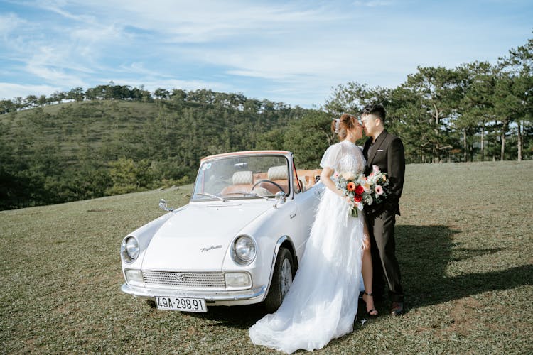 Young Asian Couple Kissing Near Retro Car In Hillscape