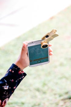 A person holds a smartphone with a clip-on lens outdoors.