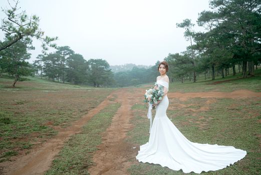 一位身着白色婚纱、手捧花束的浪漫女子，正站在绿草如茵的人行道上，面向镜头