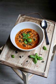 A bowl of tomato soup garnished with basil and seeds on a wooden tray.