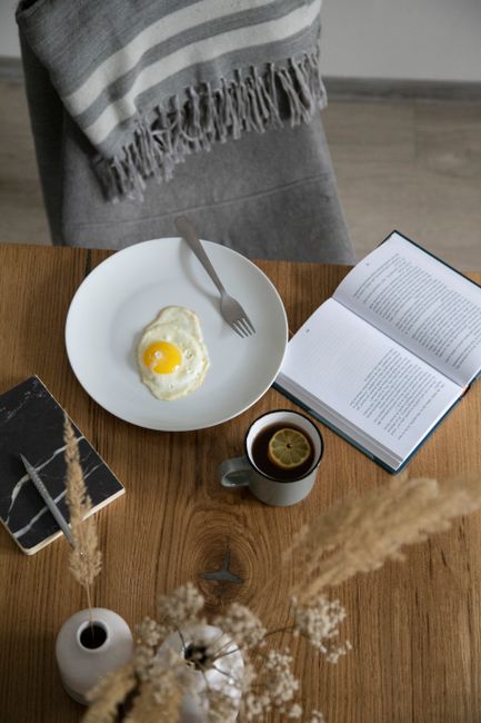 A cozy breakfast scene with an egg, tea, and open books on a wooden table.