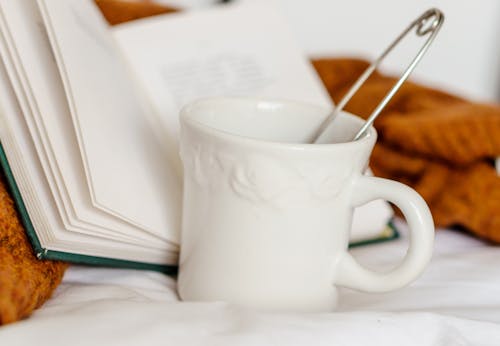 Mug with beverage and book on bed