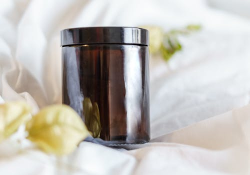 Dark glass jar near decorative plants on white fabric at light cozy home