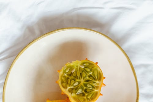 Top view of fresh kiwano on white plate on fabric in light room