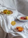 Bright ripe halves of kiwano in bowl near delicious cut orange and grapefruit on creased textile